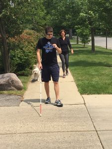 Alan Brint, who is blind, is trailed by his mother Betsy and his dog Mo, tries out his new Aira glasses. Aira’s platform works on a wearable device similar to Google glass, that can be paired with a smart phone. The tiny camera mounted on the device [cool sunglasses] provides instant feedback to a trained Aira agent who can safely guide [a wearer] in any activity. Alan was navigating his way to his local train station using an unfamiliar route as a test of the technology.