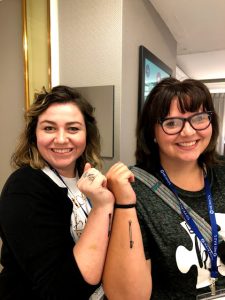two young women with matching white cane tattoos on their forearms